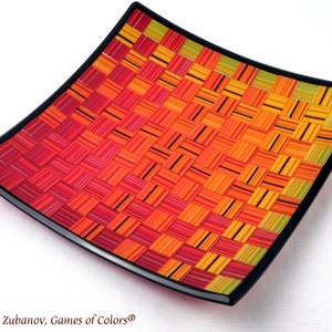 May include: A square glass serving dish with a black rim. The dish is decorated with a woven pattern of red, orange, and yellow glass strips.