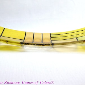Puede incluir: Un plato de vidrio amarillo con un patr&oacute;n geom&eacute;trico de l&iacute;neas negras. El plato es curvo y tiene un ligero brillo.