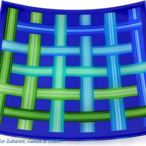May include: A blue glass serving dish with a woven pattern of green and blue stripes. The dish is slightly curved and has a rounded edge.
