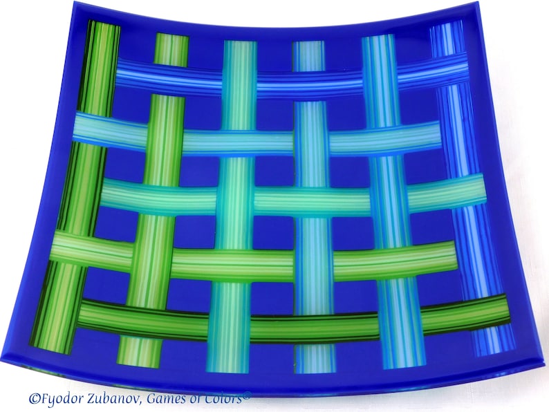 May include: A blue glass serving dish with a woven pattern of green and blue stripes. The dish is slightly curved and has a rounded edge.