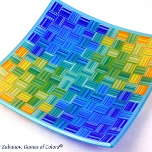 May include: A square glass serving dish with a woven pattern in shades of blue, green, and yellow. The dish has a light blue rim.