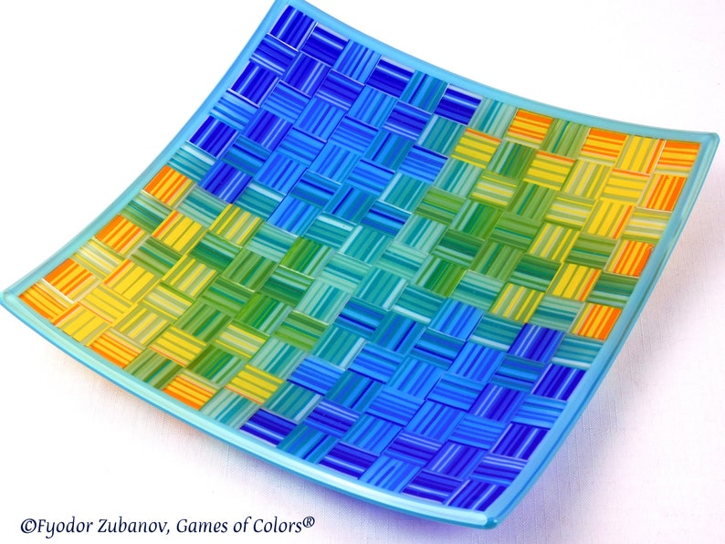 May include: A square glass serving dish with a woven pattern in shades of blue, green, and yellow. The dish has a light blue rim.