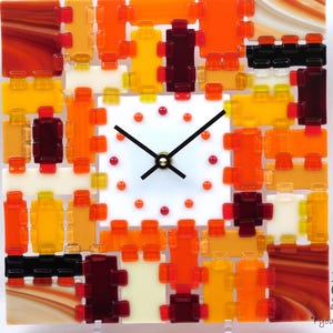 Peut inclure: Horloge murale carrée avec un cadran blanc et des aiguilles noires. L'horloge est décorée d'une mosaïque de pièces de verre orange, jaune et marron. L'horloge a un design moderne et convient à la décoration intérieure.