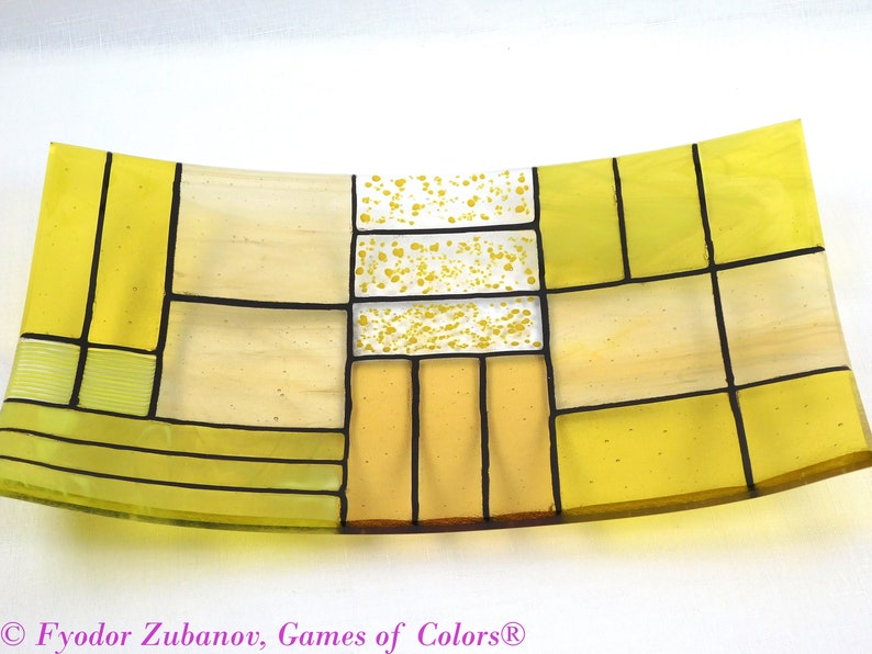 Puede incluir: Un plato de servir de vidrio amarillo con un dise&ntilde;o geom&eacute;trico. El plato est&aacute; hecho de vidrio transparente con acentos amarillos y blancos. El plato est&aacute; ligeramente curvado y tiene un dise&ntilde;o moderno.