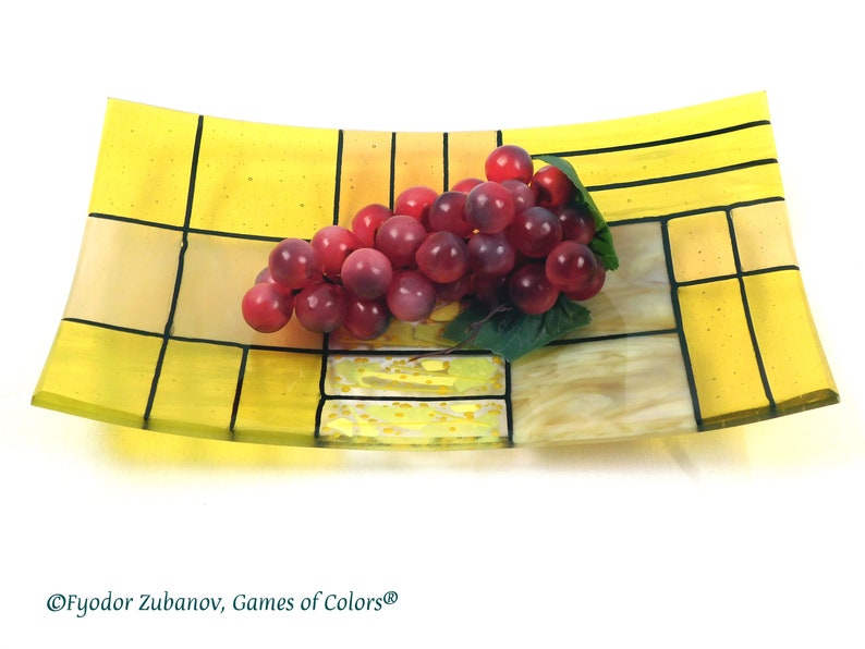 Puede incluir: Un plato de servir de vidrio amarillo con l&iacute;neas negras que forman un patr&oacute;n de cuadr&iacute;cula. Un racimo de uvas rojas se encuentra en el plato.