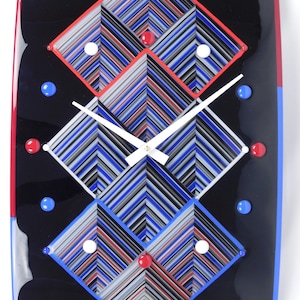 May include: A rectangular wall clock with a black background and a geometric design. The clock face features three diamond shapes with red, white, blue, and gray stripes. Red, white, and blue accents are placed around the clock face. The clock hands are white.