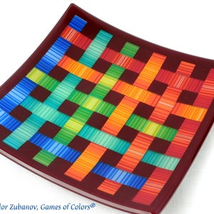 May include: A square glass plate with a woven pattern in shades of blue, green, yellow, orange, and red. The plate has a dark red border.