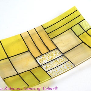 Puede incluir: Un plato rectangular de vidrio con un patr&oacute;n geom&eacute;trico de cuadrados amarillos y negros. El plato tiene una forma ligeramente curvada y est&aacute; hecho de vidrio transparente.