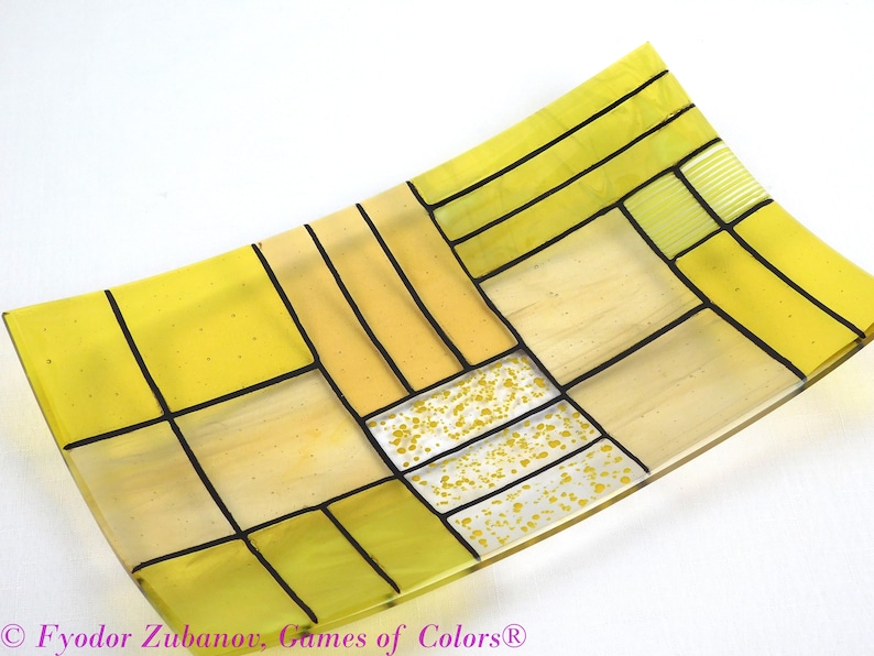 Puede incluir: Un plato rectangular de vidrio con un patr&oacute;n geom&eacute;trico de cuadrados amarillos y negros. El plato tiene una forma ligeramente curvada y est&aacute; hecho de vidrio transparente.