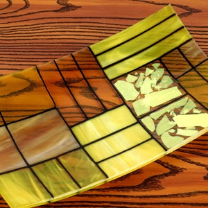 Puede incluir: Un plato rectangular de vidrio con un patr&oacute;n geom&eacute;trico de piezas de vidrio amarillo y marr&oacute;n. El plato tiene un borde ligeramente curvado y est&aacute; hecho de vidrio emplomado.