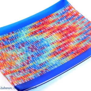 May include: A rectangular glass serving dish with a blue border and a colorful mosaic pattern in the center. The mosaic pattern is made up of small squares of glass in various shades of red, orange, yellow, green, blue, and white.