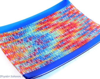 Könnte beinhalten: Eine rechteckige Glasservierplatte mit einem blauen Rand und einem bunten Mosaikmuster in der Mitte. Das Mosaikmuster besteht aus kleinen Quadraten aus Glas in verschiedenen Schattierungen von Rot, Orange, Gelb, Grün, Blau und Weiß.