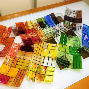 Puede incluir: Surtido de bandejas de servir de vidrio de colores con patrones geométricos. Las bandejas están hechas de vidrio emplomado y presentan una variedad de colores, incluyendo rojo, naranja, amarillo, verde, azul y morado.