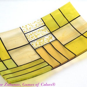 Puede incluir: Un plato de servir de vidrio amarillo con un patr&oacute;n geom&eacute;trico de cuadrados y rect&aacute;ngulos. El plato est&aacute; hecho de vidrio transparente con un tinte amarillo y tiene l&iacute;neas negras que delinean los cuadrados y rect&aacute;ngulos. El plato est&aacute; ligeramente curvado y tiene una superficie lisa.