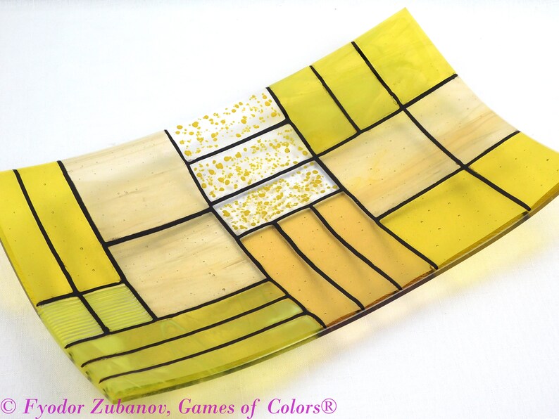 Puede incluir: Un plato de servir de vidrio amarillo con un patr&oacute;n geom&eacute;trico de cuadrados y rect&aacute;ngulos. El plato est&aacute; hecho de vidrio transparente con un tinte amarillo y tiene l&iacute;neas negras que delinean los cuadrados y rect&aacute;ngulos. El plato est&aacute; ligeramente curvado y tiene una superficie lisa.