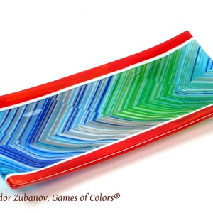 Puede incluir: Un plato de servir rectangular de vidrio con un borde rojo y un patrón de rayas en tonos de azul, verde y gris.