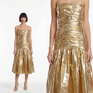 May include: A gold strapless dress with a ruched bodice and a flared skirt. The knee-length dress has a metallic finish. The model is wearing gold high heels. The dress is approximately 100 cm in length.
