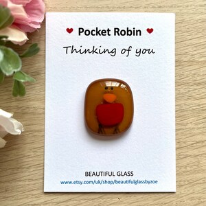 Pu&ograve; includere: Una piccola figurina di vetro di un pettirosso, con un corpo marrone, petto rosso e becco arancione. La figurina &egrave; su una carta bianca con il testo "Pocket Robin Thinking of you" e "BEAUTIFUL GLASS www.etsy.com/uk/shop/beautifulglassbyzoe".