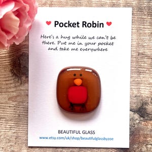Fused glass robin handmade with brown body, red breast, orange beak and black dots for eyes and stripes for feet. Stuck to a 7.5cm x 9cm piece of white card with choice of pocket hug message.