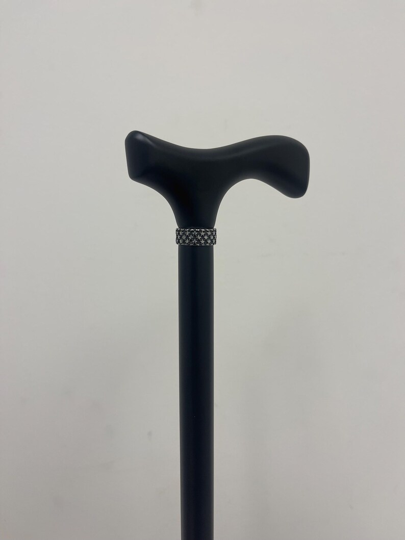 May include: A black wooden walking stick with a decorative silver band around the handle.