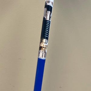 May include: A white and blue walking cane with a black and silver design on the upper portion. The cane has a black rubber tip.