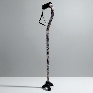 May include: A patterned walking cane with a black handle and a black quad base. The cane's shaft is covered in a colorful pattern. A black strap is attached to the handle. The cane is designed to provide support while walking.