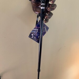 May include: A black and silver walking cane with a handle shaped like a hand. The handle has a black and silver design. The cane is black with a silver accent. A tag is attached to the cane.