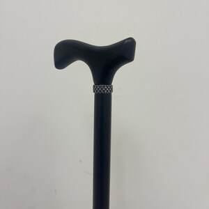 May include: A black wooden walking cane with a T-shaped handle and a decorative silver band.