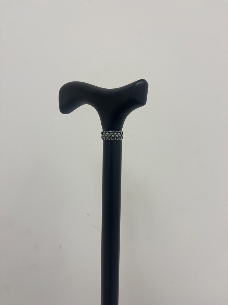 May include: A black wooden walking cane with a T-shaped handle and a decorative silver band.