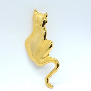 May include: A gold-colored metal cat figurine. The cat is sitting with its tail curled around its body.