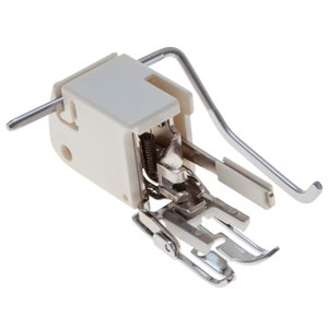 May include: A white and silver sewing machine foot with a lever and a spring. The foot is designed for sewing a rolled hem.