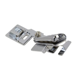 May include: A silver sewing machine foot attachment with a curved metal guide. The foot is designed for creating a rolled hem.