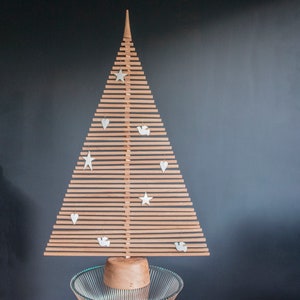 May include: A wooden Christmas tree with a natural wood finish. The tree is decorated with white stars, hearts, and doves. The tree is standing on a clear glass base.