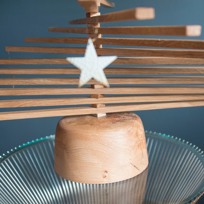 May include: A wooden Christmas tree made of stacked slats with a white star ornament hanging from the top. The tree is sitting on a glass plate.