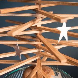 May include: A wooden Christmas tree made of stacked slats with white star ornaments hanging from the branches.