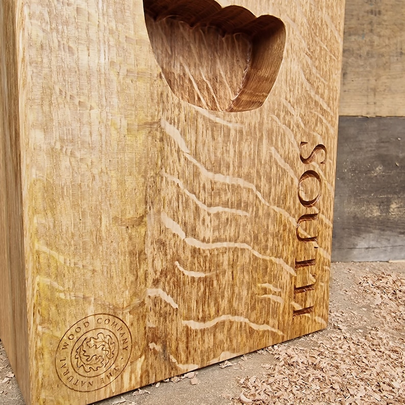 May include: A solid, rectangular wooden block with a carved handle. The wood has a natural grain pattern and is engraved with the word "SOUL" and the logo of "THE NATURAL WOOD COMPANY". The block is light brown with a rough texture.