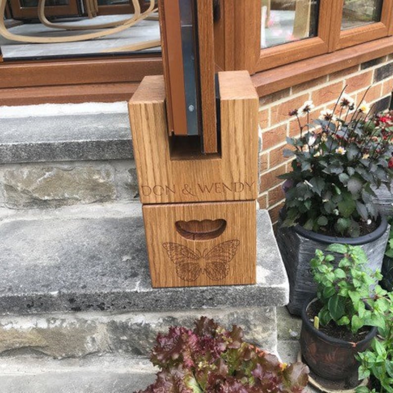 May include: A wooden, personalized mailbox post with the names "DON & WENDY" engraved on the front. The lower section features a butterfly design. The post is made of light brown wood and is sitting on stone steps.