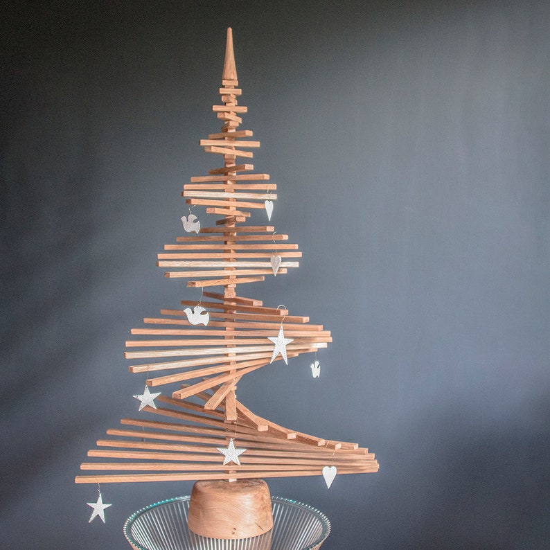 May include: A wooden Christmas tree made of stacked slats with white star and bird ornaments hanging from it. The tree is on a clear glass base.