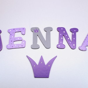May include: Purple and gray wooden letters spelling out the name "JENNA" with a purple crown with rhinestones.
