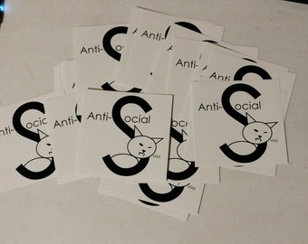 May include: A stack of white square stickers with a black outline of the letter "S" and a cartoon cat inside the letter. The text "Anti-social" is printed on the stickers. The cat has a small mouth and the word "Hiss" is printed below the cat.