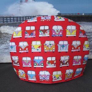 May include: Red fabric teapot cover with a pattern of colorful vintage Volkswagen vans.
