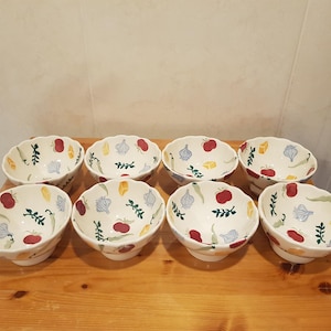 May include: Set of eight white ceramic bowls with a scalloped edge. The bowls feature a colorful pattern of vegetables and fruits, including red tomatoes, green peppers, and purple onions.