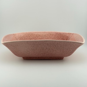 May include: A rectangular ceramic bowl with a soft pink base color and a darker pink speckled pattern throughout. The bowl features flared sides, rounded corners, and a smooth, matte-textured finish on the exterior and interior surfaces.