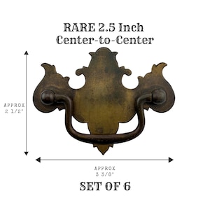 May include: A brass drawer pull with a decorative backplate and a swinging handle. Text reads: RARE 2.5 Inch Center-to-Center, APPROX 2 1/2", APPROX 3 3/8", SET OF 6. The hardware features a dark, aged patina finish with ornate, curved edges.