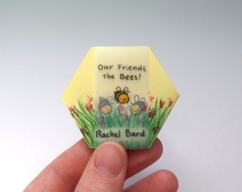 May include: A yellow hexagonal card with a green, yellow, and red floral design. Three cartoon bees are flying over the flowers. The card reads "Our Friends The Bees!" and is signed "Rachel Bard".