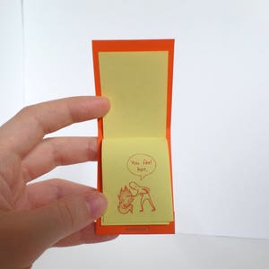 May include: A small orange card with a yellow note inside. The note has a cartoon drawing of a person with a speech bubble that says "You feel hot."