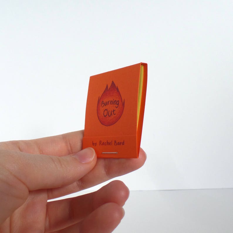 May include: A small orange booklet with a yellow spine. The cover features a red and orange flame illustration with the text "Burning Out" and "by Rachel Bard".
