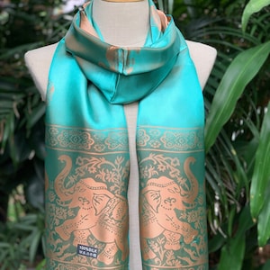 May include: A turquoise silk scarf with a gold embroidered design of elephants and floral patterns. The scarf has a fringed edge and a label that reads "100% Silk".