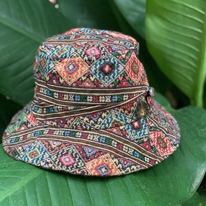 May include: A colourful bucket hat with a geometric pattern in shades of red, blue, green, and brown. The hat is made of woven fabric and has a wide brim.
