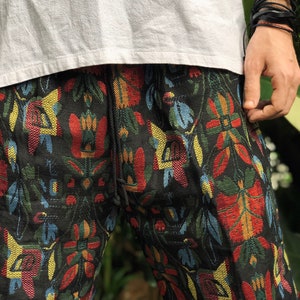 May include: Black patterned shorts with a drawstring waist. The shorts have a colourful floral design in red, yellow, blue, and green. The shorts are paired with a white t-shirt.
